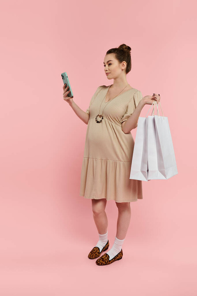 Una mujer embarazada en un vestido con un teléfono celular y bolsas de la compra. - Foto, Imagen