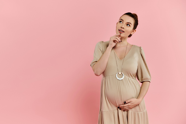 Беременная женщина в платье, позирующая на розовом фоне. - Фото, изображение
