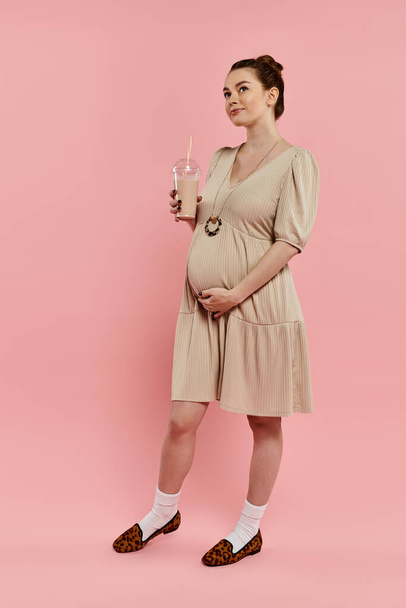 Une femme enceinte dans une robe tenant milkshake sur un fond rose. - Photo, image