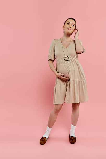 Μια λαμπερή έγκυος γυναίκα στέκεται με χάρη μπροστά σε ένα ροζ φόντο. - Φωτογραφία, εικόνα