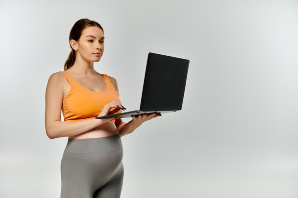 Una mujer embarazada joven y deportiva en uso activo sostiene una computadora portátil en sus manos. - Foto, imagen