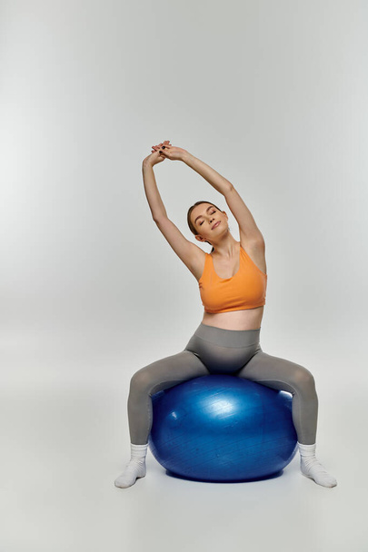 Αθλητική έγκυος γυναίκα σε ενεργό φθορά εξισορρόπηση πάνω από ένα φωτεινό μπλε μπάλα άσκησης. - Φωτογραφία, εικόνα