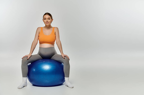 Молодая беременная женщина в активной одежде изящно балансирует на вершине яркого синего мяча для упражнений. - Фото, изображение