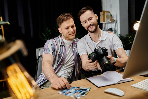 Twee stijlvolle, diverse mannen werken samen aan een project aan een bureau met een laptop en camera. - Foto, afbeelding
