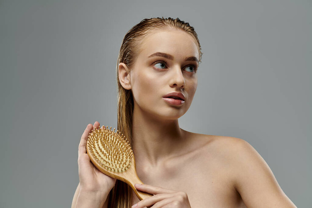 Młoda piękna kobieta demonstruje swoją rutynę pielęgnacji włosów z mokrymi włosami, trzymając szczotkę do włosów. - Zdjęcie, obraz