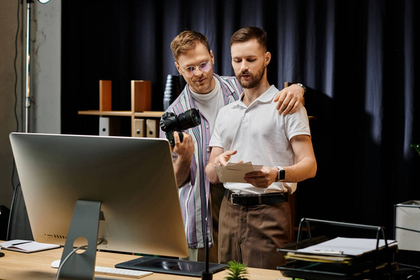 Dois homens, de traje casual, trabalham juntos em um computador em um ambiente de escritório. - Foto, Imagem