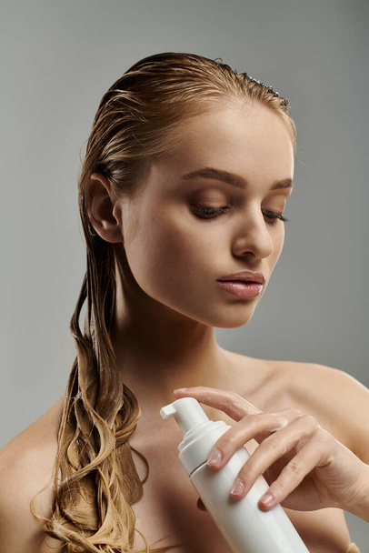 Mujer atractiva con el pelo mojado sostiene una botella de loción en sus manos, mostrando su rutina de cuidado del cabello. - Foto, imagen