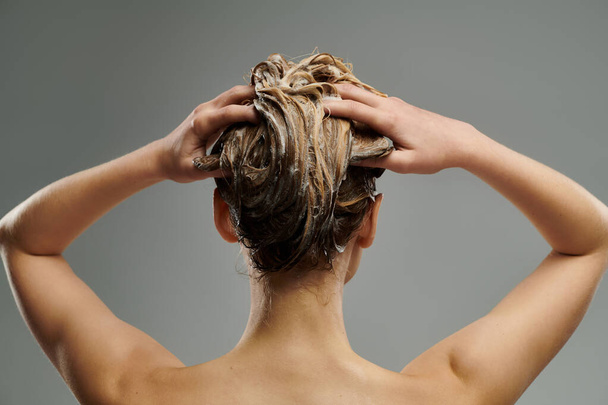 若い女性は濡れた髪で彼女のヘアケアのルーチンを示しています. - 写真・画像