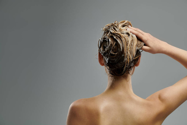 Μια νεαρή γυναίκα με ογκώδη μαλλιά παρουσιάζει ρουτίνα φροντίδας των μαλλιών της με υγρές κλειδαριές. - Φωτογραφία, εικόνα