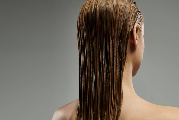 Una giovane donna mette in mostra la sua routine di cura dei capelli con bagnato, serrature fluenti. - Foto, immagini