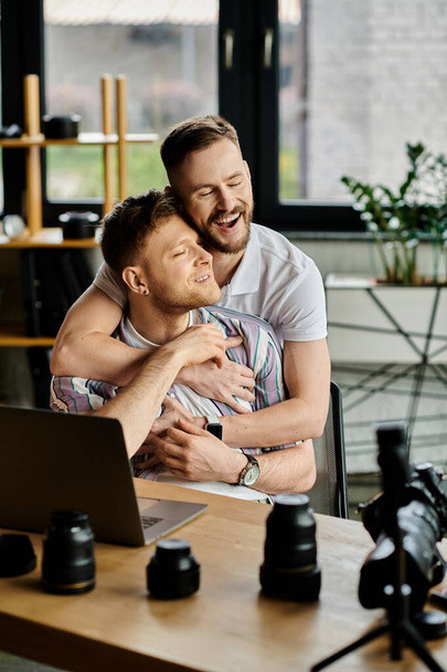 Two men in casual attire sharing a warm embrace while working in front of a laptop. - Photo, Image