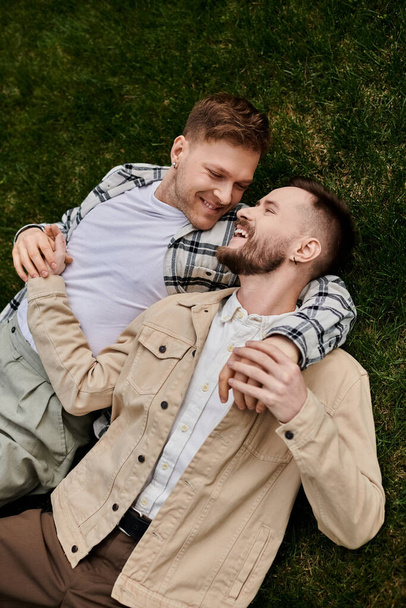 gelukkig gay paar in comfortabele kleding lounge op een weelderig groen veld. - Foto, afbeelding