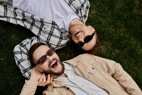 Dos hombres amorosos tendidos en la hierba en un tierno abrazo, disfrutando del aire libre. - Foto, Imagen