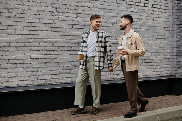 Two men in casual attire stand by a brick wall, sharing a moment of connection. - Photo, Image
