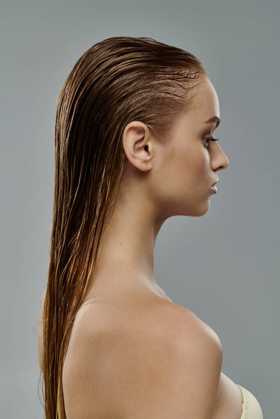 Junge Frau posiert mit nassen Haaren vor grauem Hintergrund. - Foto, Bild