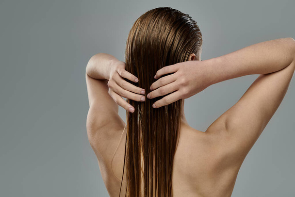 Μια γυναίκα με μακριά βρεγμένα μαλλιά ποζάροντας σε γκρι φόντο. - Φωτογραφία, εικόνα
