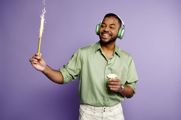 Młody Afroamerykanin w aparacie na zęby i słuchawkach z radością trzyma kubek i iskierkę. - Zdjęcie, obraz