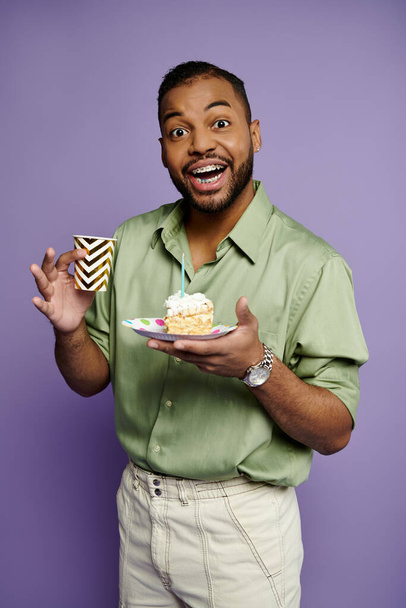 Jonge Afro-Amerikaanse man met beugels glimlachend terwijl hij een bord vasthoudt met een heerlijk stuk taart. - Foto, afbeelding