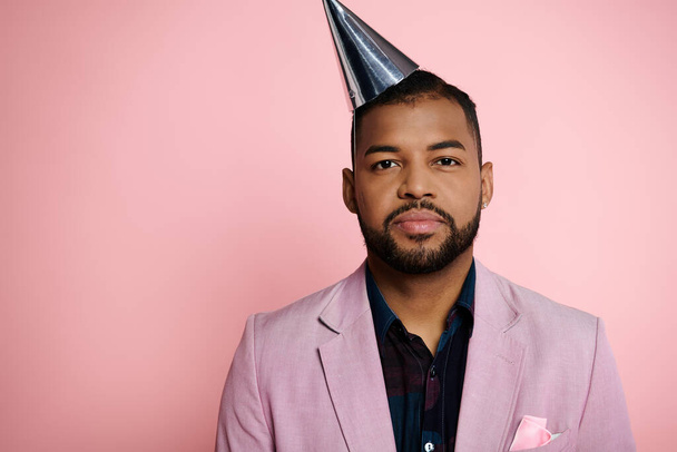 若いアフリカ系アメリカ人男性は活気に満ちたピンクの背景に対してパーティー帽子をかぶります. - 写真・画像