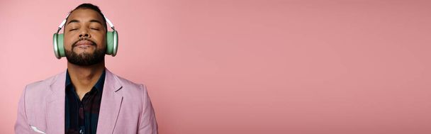 Ένας νεαρός Αφροαμερικάνος με ακουστικά στέκεται μπροστά σε ένα φωτεινό ροζ τοίχο.. - Φωτογραφία, εικόνα