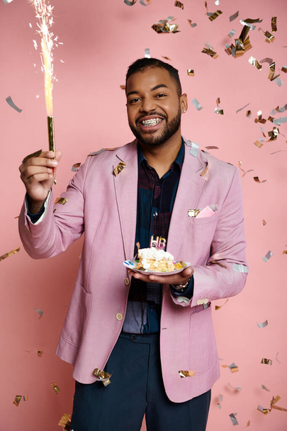 Young African American man in a pink jacket holds a sparkler on a vibrant pink background, expressing happiness. - Photo, Image