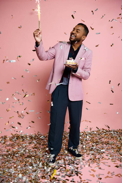 鮮やかな背景に対してピンクのジャケットで幸せな若いアフリカ系アメリカ人男性が保持する明るいスパークラー. - 写真・画像