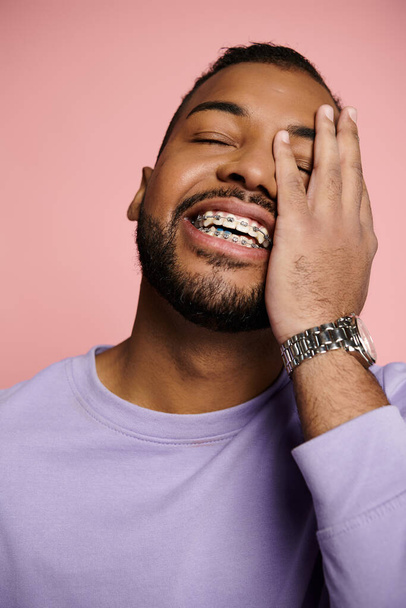 Een jonge Afro-Amerikaanse man die fel glimlacht, zijn beugel laat zien, tegen een levendige roze achtergrond. - Foto, afbeelding