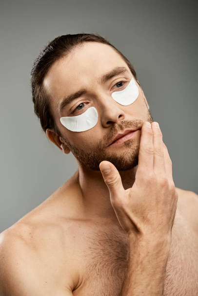 Schöner, hemdloser Mann mit Augenklappen und Bart, der vor grauer Studiokulisse Intrigen ausstrahlt. - Foto, Bild