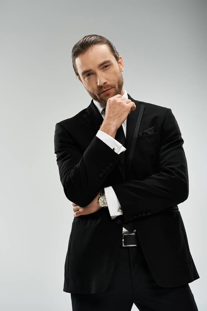 A bearded businessman in a stylish suit and tie strikes a confident pose against a grey studio background. - Foto, Bild