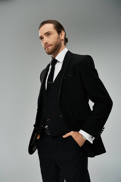 Knappe, bebaarde zakenman in pak en stropdas poseert zelfverzekerd in een studio tegen een grijze achtergrond. - Foto, afbeelding