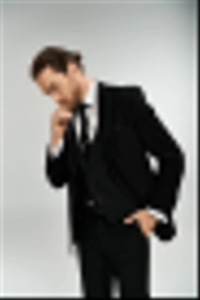 Un hombre de negocios barbudo con un traje elegante toma una postura confiada contra un fondo gris del estudio. - Foto, imagen