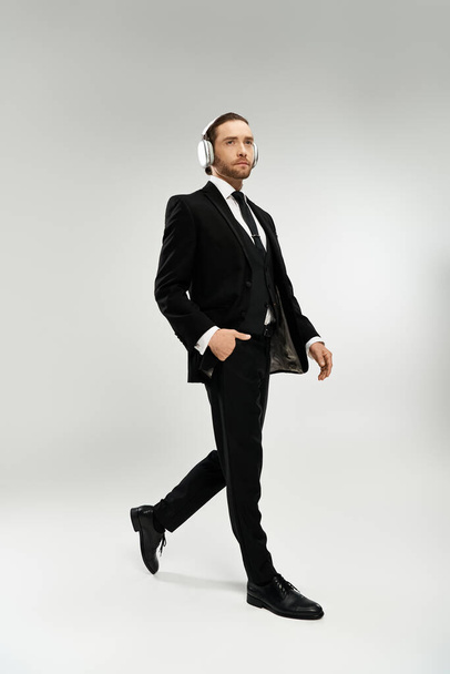 Homem de negócios barbudo em um terno elegante, usando fones de ouvido, passeando com confiança. - Foto, Imagem