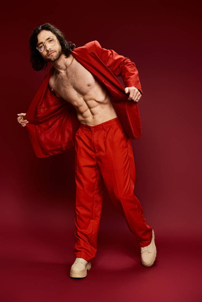 Un bell'uomo in un abito rosso vibrante posa fiducioso in uno studio senza camicia. - Foto, immagini