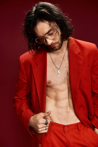 Handsome man confidently poses in a red suit without a shirt in a stylish studio setting. - Фото, зображення