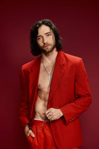 Красивий чоловік в разючому червоному костюмі, без сорочки, вдарив впевнену позу в студійній обстановці. - Фото, зображення