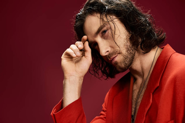 Um homem bonito com cabelo fluindo bate uma pose em uma jaqueta vermelha vibrante. - Foto, Imagem
