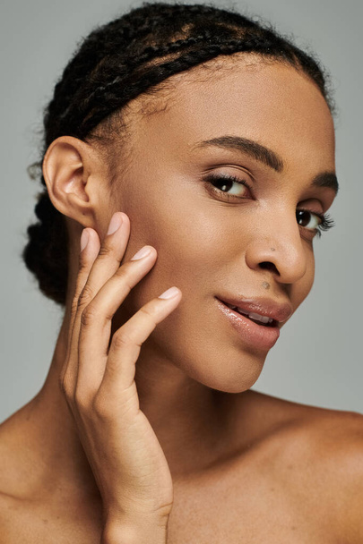 Giovane donna afroamericana con trecce posa fiduciosa, prendersi cura della sua pelle su uno sfondo grigio. - Foto, immagini