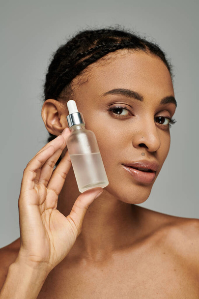 Gyönyörű fiatal afro-amerikai nő szíj nélküli felső tartja szérum az arcához koncentrált gondossággal. - Fotó, kép