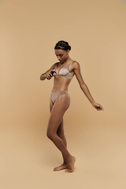 Beautiful, slim African American woman standing confidently in a bikini against a beige backdrop. - Photo, Image