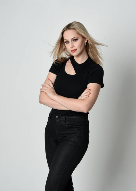 Nahaufnahme Porträt einer schönen blonden Frau in modernem schwarzen Hemd und Lederhose. Selbstbewusste Stehhaltung mit Handgesten, isoliert auf weißem Studiohintergrund. - Foto, Bild