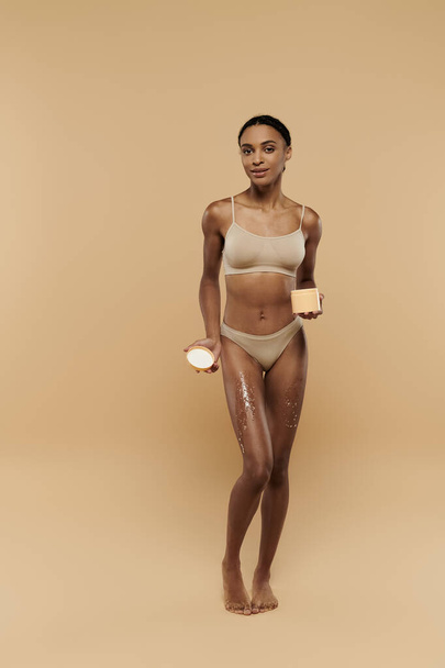 An African American woman in a bikini with sugar scrub on legs exuding tranquility. - Фото, изображение