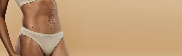 Elegante Afro-Amerikaanse vrouw in wit bikinitopje op een beige achtergrond. - Foto, afbeelding