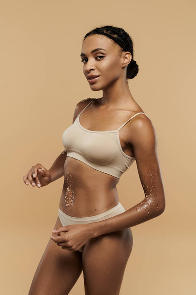 Afroamerikanerin trägt ein Bikini-Oberteil und Höschen mit Anmut und Selbstbewusstsein auf neutralem Hintergrund. - Foto, Bild