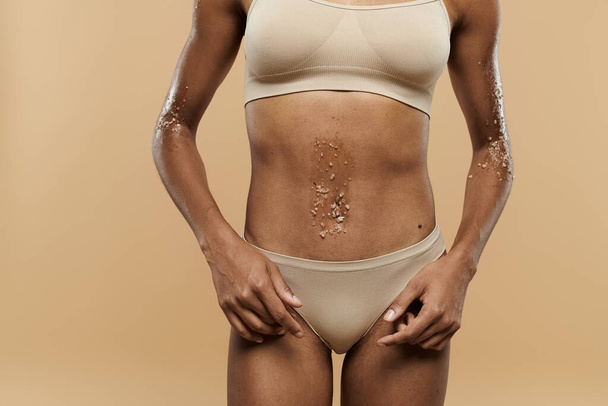 Pretty, slim African American woman standing in bra and panties on beige background. - Foto, immagini
