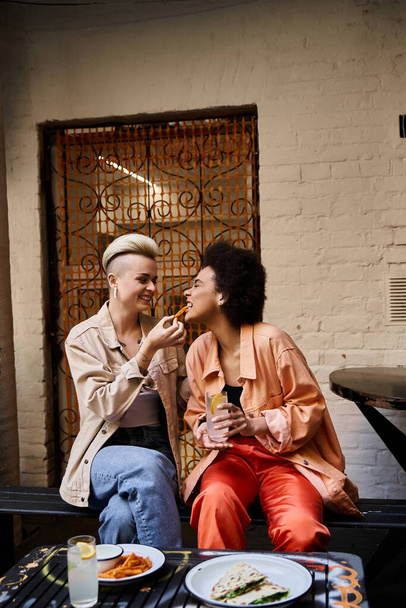 Una coppia eterogenea di lesbiche che si godono un pasto insieme su una panchina. - Foto, immagini