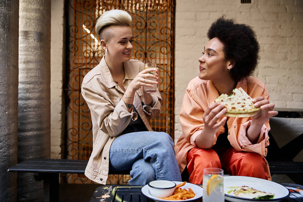 Dwie różnorodne, piękne lesbijki siadają przy stole, delektując się wspólnym posiłkiem. - Zdjęcie, obraz