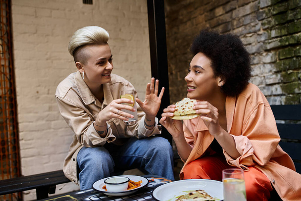 Dos hermosas mujeres de diferentes etnias se sientan juntas en una mesa, compartiendo una comida en un acogedor café. - Foto, imagen