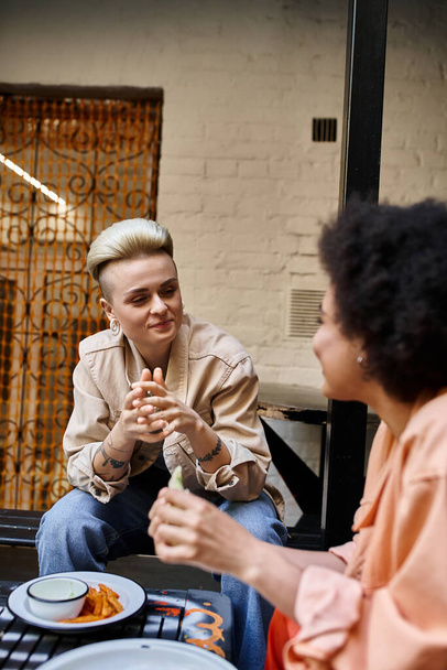 Twee vrouwen betrokken bij een levendig gesprek aan een cafe tafel. - Foto, afbeelding