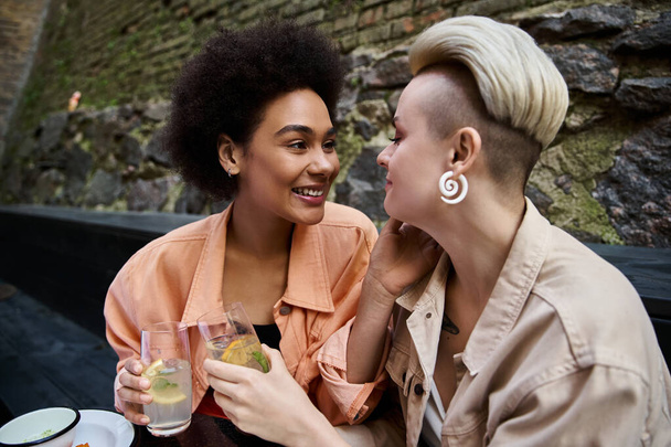 Zwei unterschiedliche Frauen genießen ein Date in einem gemütlichen Café, sitzen eng beieinander und unterhalten sich. - Foto, Bild