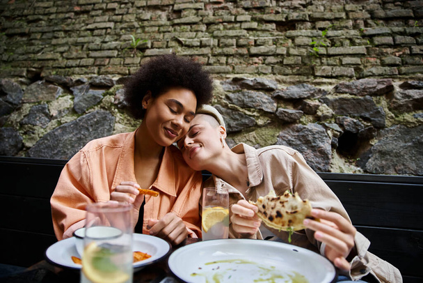 Різноманітна, красива пара жінок сидить за столом, насолоджуючись їжею разом. - Фото, зображення